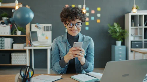 A smiling small business owner checking a phone at an office desk