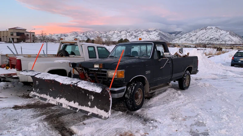 Pickup trucks fitted with snow plow blades in a snowy lot at dusk, the kind of vehicles snow removal insurance often covers