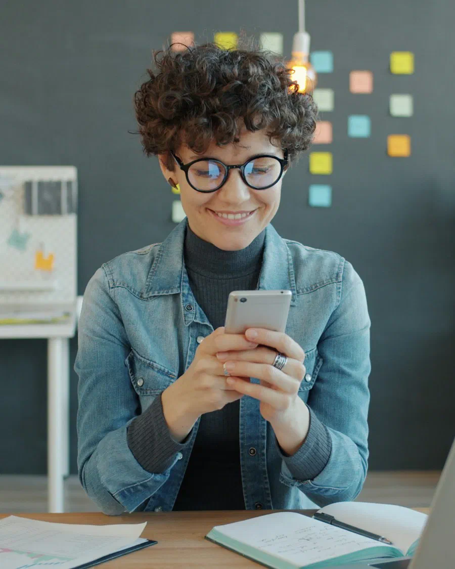 A smiling small business owner checking a phone at an office desk