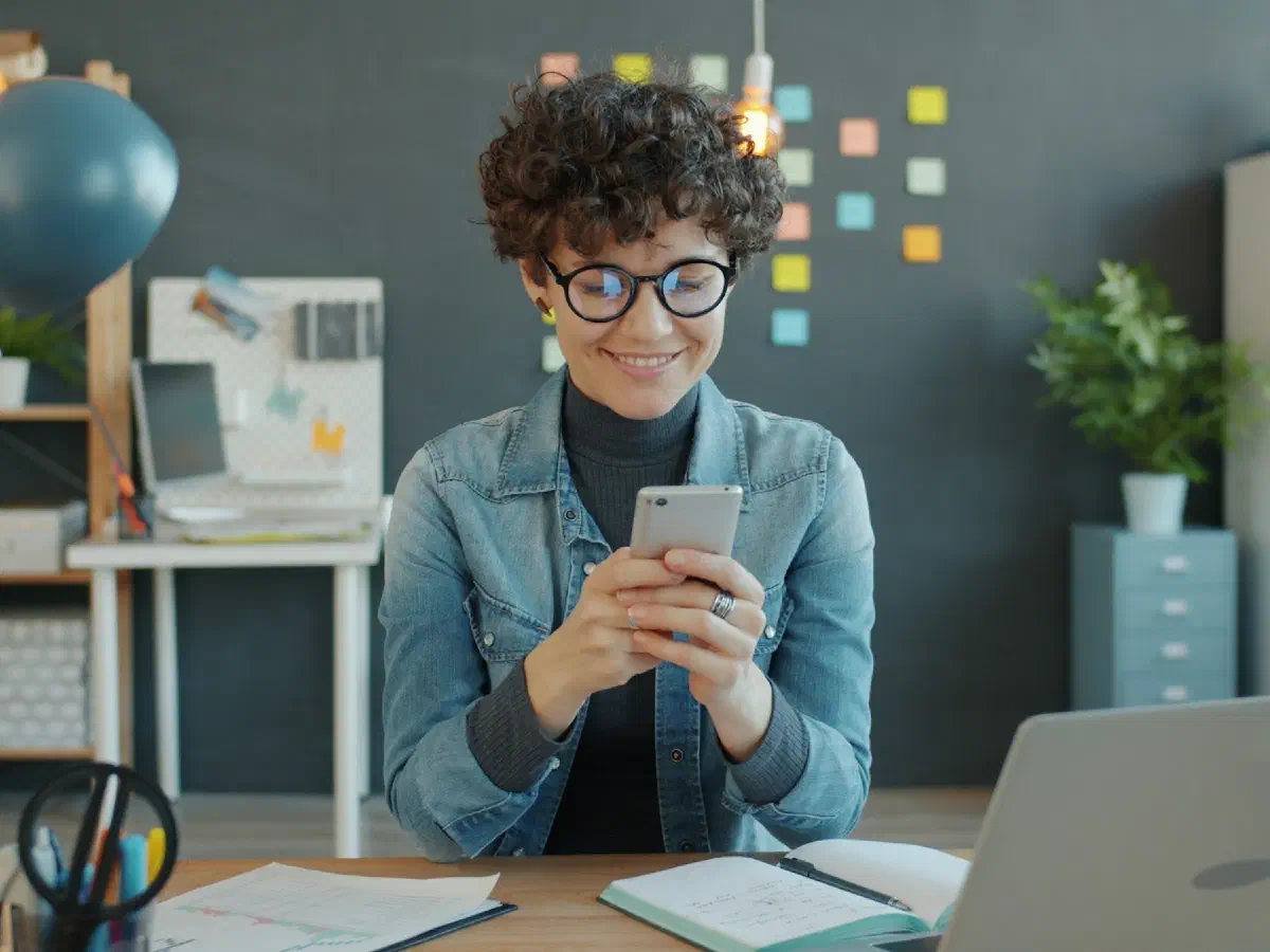 A smiling small business owner checking a phone at an office desk